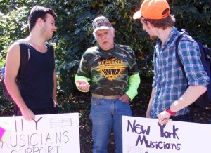 Dennis Bugash (centro), minero por 25 años, de Pennsylvania, habla con músicos Dean Mahoney (izq.), y Harry D’Agostino, en acto por pensiones en Columbus, Ohio, el 12 de julio. 