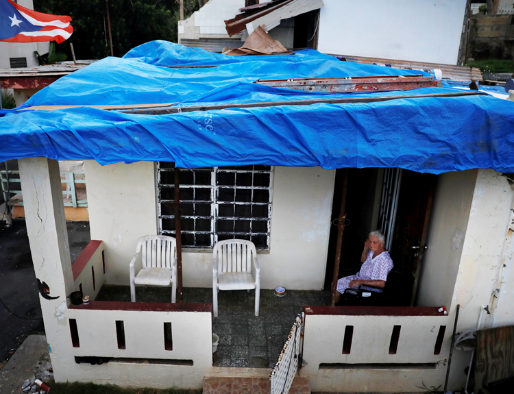 Lucila Cabrera, 86, sits on porch of her house near Barceloneta, Puerto Rico, still covered with plastic tarp. One year after Hurricane Maria, tens of thousands of homes still have not gotten funds or help to build a new roof. FEMA has denied one third of requests for aid.