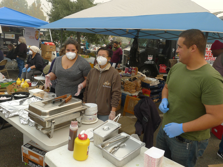 Volunteers wearing masks to keep out smoky air serve food to fire survivors at Walmart encampment Nov. 15. Hundreds of workers are volunteering in face of government inaction.