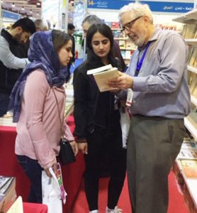 Above, Ögmundur Jónsson from U.K. talks at Pathfinder booth with Mohammed Ja’far, who is rebuilding library destroyed by Islamic State in village near Mosul. At left of photo is Pathfinder volunteer Martin Hill from U.K. Below, Steve Penner of Canada discusses Pathfinder titles with fair visitors.