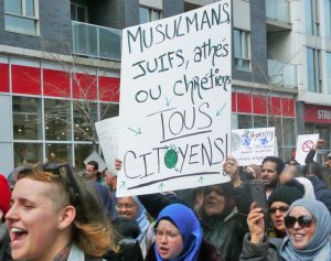 Sign reads, “Muslims, Jews, atheists or Christians. All citizens!” Thousands protest in Montreal April 7 against bill banning public sector workers from wearing religious symbols at work.