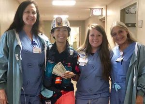 Chinese restaurant owner Joyce Cheng, in miner’s helmet and jacket, with nurses at Harlan Appalachian Regional Healthcare July 11. She ran 50 miles “asking every person for a dollar” for laid-off Blackjewel miners, raising over $5,000 for miners’ families she knows.