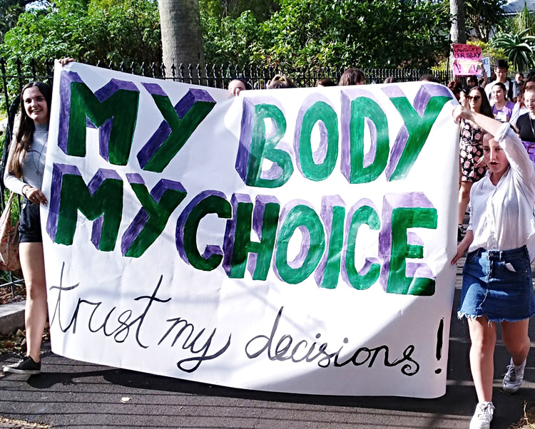 Holly Wakelin, left, and Lucy Mackenzie, right, two young women who helped lead recent actions for women’s right to abortion, hold banner at Auckland Feb. 18 march. After decades of mobilizations, New Zealand’s parliament adopted law legalizing abortion March 18.