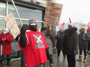 Airline catering workers organized by Unifor Local 698 protest eight-week lockout by Gate Gourmet at airport in Montreal Dec. 31. Placard on right says, “If we are on the outside, something is wrong on the inside.” One on left says, “You don’t get rich on our earnings.”