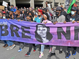 Tamika Palmer, center, marches behind banner with portrait of her daughter Breonna Taylor, in Louisville March 13 on first anniversary of fatal shooting by police. Hundreds who took part demanded the cops responsible face criminal charges over her killing.