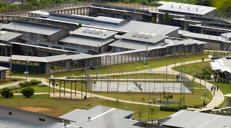 Above, immigration detention center on Christmas Island, remote Australian territory in Indian Ocean. Hundreds of “501 detainees” are imprisoned there, facing deportation under Canberra’s law using “character grounds” to cancel visas of long-term residents. The law especially targets workers from New Zealand. Left, a fire at compound Jan. 10 after several days of sit-in protesting indefinite detention without family visits or contact with anyone.