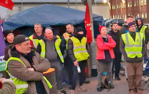 Unite union members on strike in Manchester, England, against CHEP pallet company meet, listen to transport union officer bringing solidarity Jan. 14. Strikers are demanding 5% pay raise.