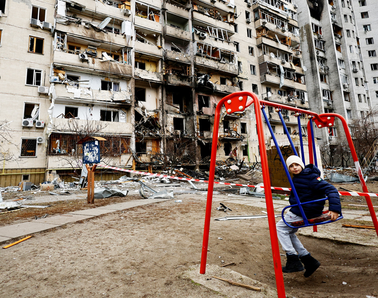 A child sits on swing near bombed out buildings in Kyiv, Ukraine, Feb. 25, the day after invasion by Russian forces started. Fought to standstill by Ukraine, Moscow is destroying urban centers.