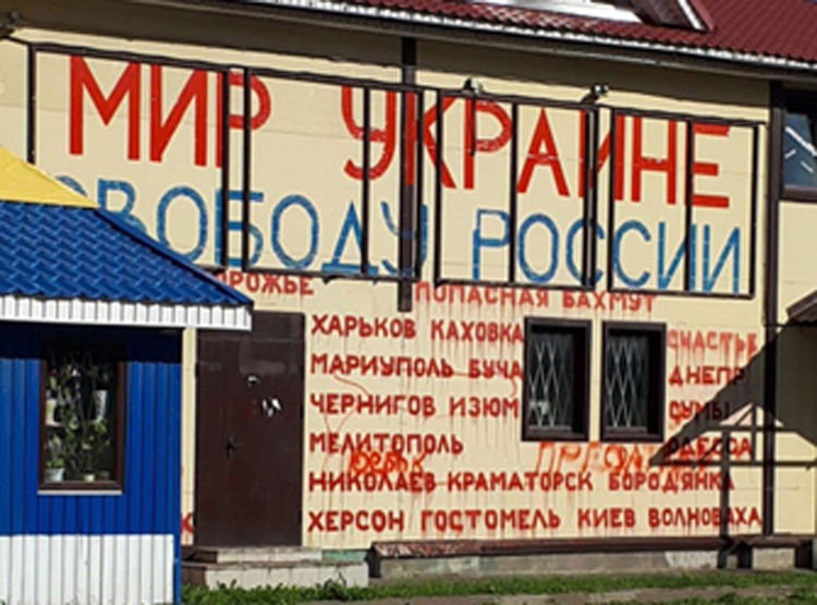 “My neighbors fully support me,” Dmitry Skurikhin, inset, says. Roof of his shop in northwest Russia, July 19, is painted in Ukrainian colors. Under slogan, “Peace to Ukraine, freedom for Russia!” are names of “towns, cities of Ukraine suffering” from Russian military attacks. Police charged him several times, but he and his signs remain.