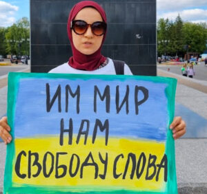 Despite mass arrests against anti-war demonstrations across Russia, protests continue. In recent public action in square in Ufa, in the Volga region, Elmira Rahmatullina holds sign in Ukrainian colors of blue and yellow, saying, “Give them peace, and us, freedom of speech.”
