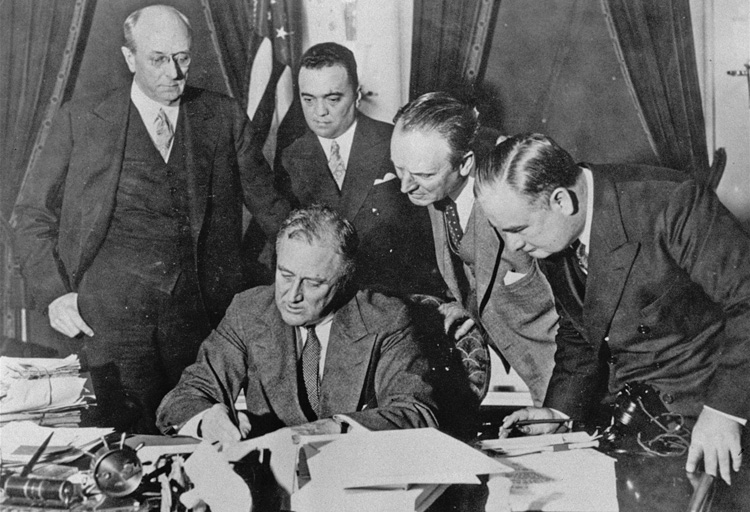 Democrat President Franklin Roosevelt, with FBI Director J. Edgar Hoover, to right of flag, signs 1934 bill increasing federal police powers for use against the labor movement.