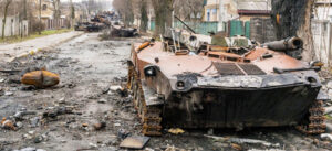 Wrecked Russian tank convoy, above, hit by volunteer fighters as Moscow’s early assault neared Kyiv. Inset, former journalist Tetyana Chornovol who got and fired the anti-tank weapon that destroyed the armored column. Working people like her joined soldiers to push Russia’s invasion back in the most consequential battle in Europe since World War II.