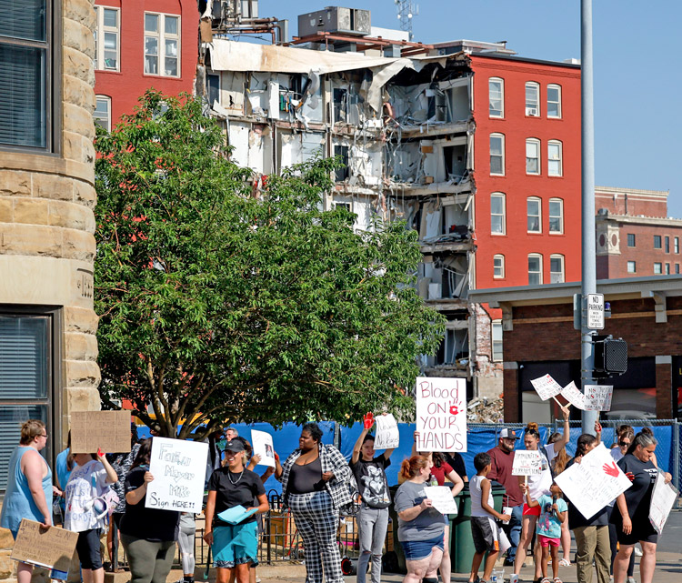Protest June 7 at Davenport, Iowa, City Hall, with partially collapsed apartment building in back, demands owner, city officials be held responsible for deaths, injuries, loss of homes.