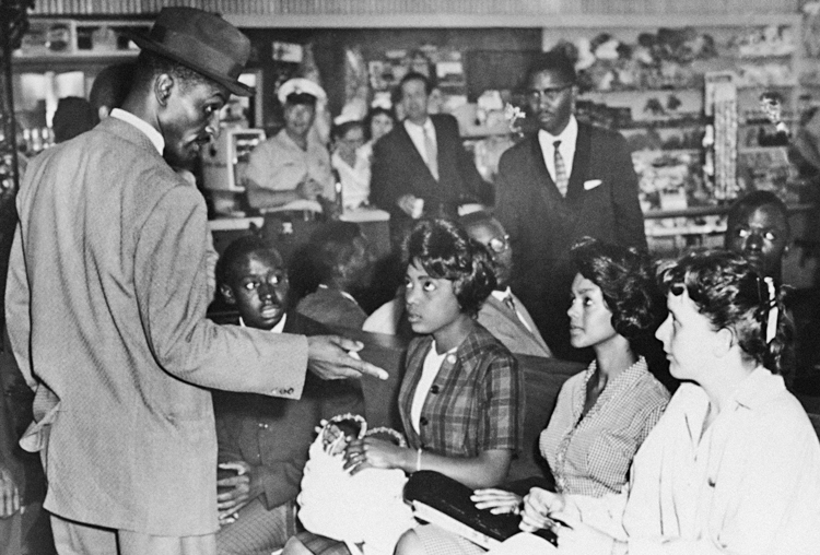 Above, Rev. Fred Shuttlesworth, left, speaks with Freedom Riders, seated from left, Charles Butler, Catherine Burks-Brooks, Lucretia Collins and Salynn McCollum in white waiting room in Birmingham, Alabama, bus station, May 17, 1961. Inset, Burks-Brooks smiles in mug shot after being arrested in Jackson, Mississippi, 11 days later.
