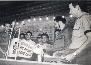 Minister of Industry Che Guevara presents literacy drive banner at paint factory in Havana in November 1961. Don’t try to set “a world record,” he said, but “combine study and work.”
