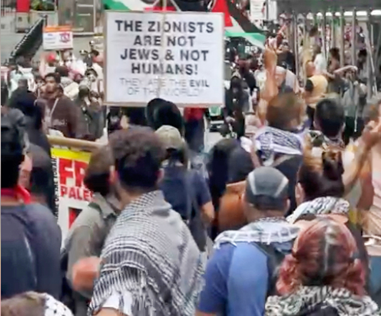 Protesta contra exhibición sobre Festival Nova, Nueva York, junio 10, muestra odio antijudío. Manifestantes afirmaron que la brutalidad del pogromo de Hamás el 7 de octubre mostrado en la exhibición era “propaganda sionista”. Cartel dice “sionistas no son judíos y no son humanos”.