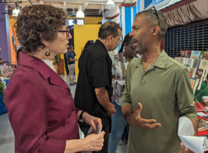 Rachele Fruit, candidata del PST para presidente de EE.UU., habla con Harold Etimé en Feria del Libro en Miami, mayo 5. El PST se opone a intervenciones de EE.UU. desde Haití a la OTAN.