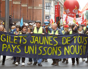 Over 100,000 marched in some 250 rallies across France May 1, 2022, including in Toulouse, above, demanding President Macron drop his move to raise workers’ retirement age. Protesters called themselves “gilets jaunes.” Banner reads, “Yellow vests of all countries, unite!”