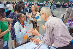 Discussions at Pathfinder Press booth at 2024 National Federation of the Blind convention in Orlando, Florida. Volunteers introduced Pathfinder books available in Braille and large print.