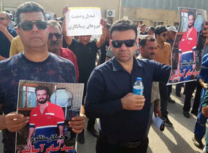 Oil workers protesting in Gachsaran, Iran Aug. 17, hold photo of Saber Asayesh, who died because of company disdain for workers’ lives, denial of heath care to contract workers.
