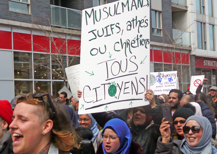 2019 protest against Law 21 in Montreal. Placard reads, “Muslims, Jews, atheists and Christians are all citizens.” New bill would extend discriminatory restrictions on wearing religious symbols at work, day care centers, immigration proceedings, French-language classes and more.