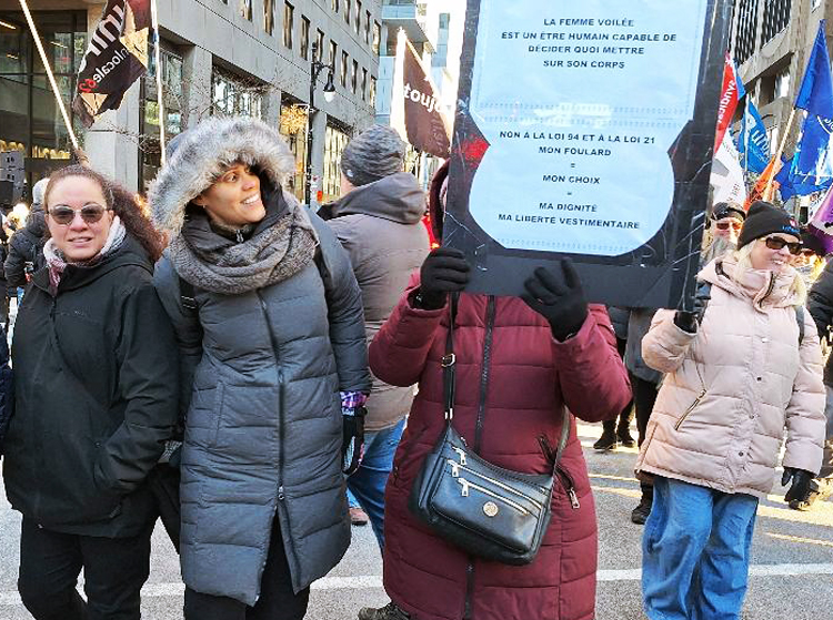 Manifestation de 50 000 personnes à Montréal le 29 novembre contre de nouvelles lois anti-ouvrières. La syndicaliste Nawal Chi tient une pancarte sur laquelle on peut lire : « Non à la loi 94 et à la loi 21. Mon foulard, mon choix, ma dignité, ma liberté vestimentaire. »